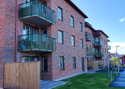 Sockenmagasinet i klassisk tegelfasad med grönmålade balkonger och detaljer, belägna i ett lugnt bostadsområde.