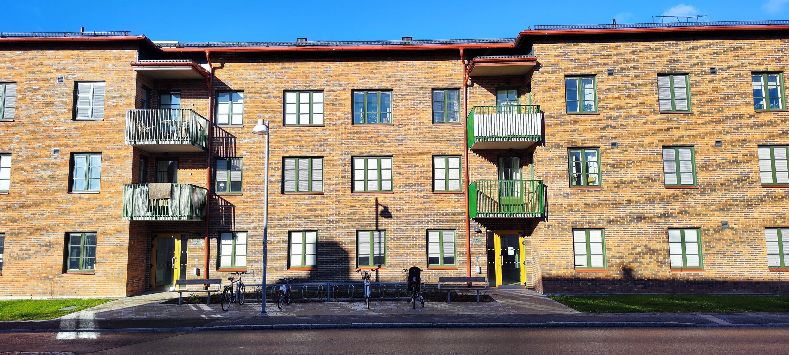 Sockenmagasinet med gröna fönster och balkonger mot gatan. Entréer med gula dörrar, cykelställ och bänkar framför huset.