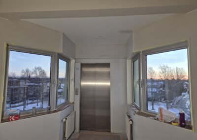 Hissdörr mellan två fönster i utrymme med pågående målningsarbete.