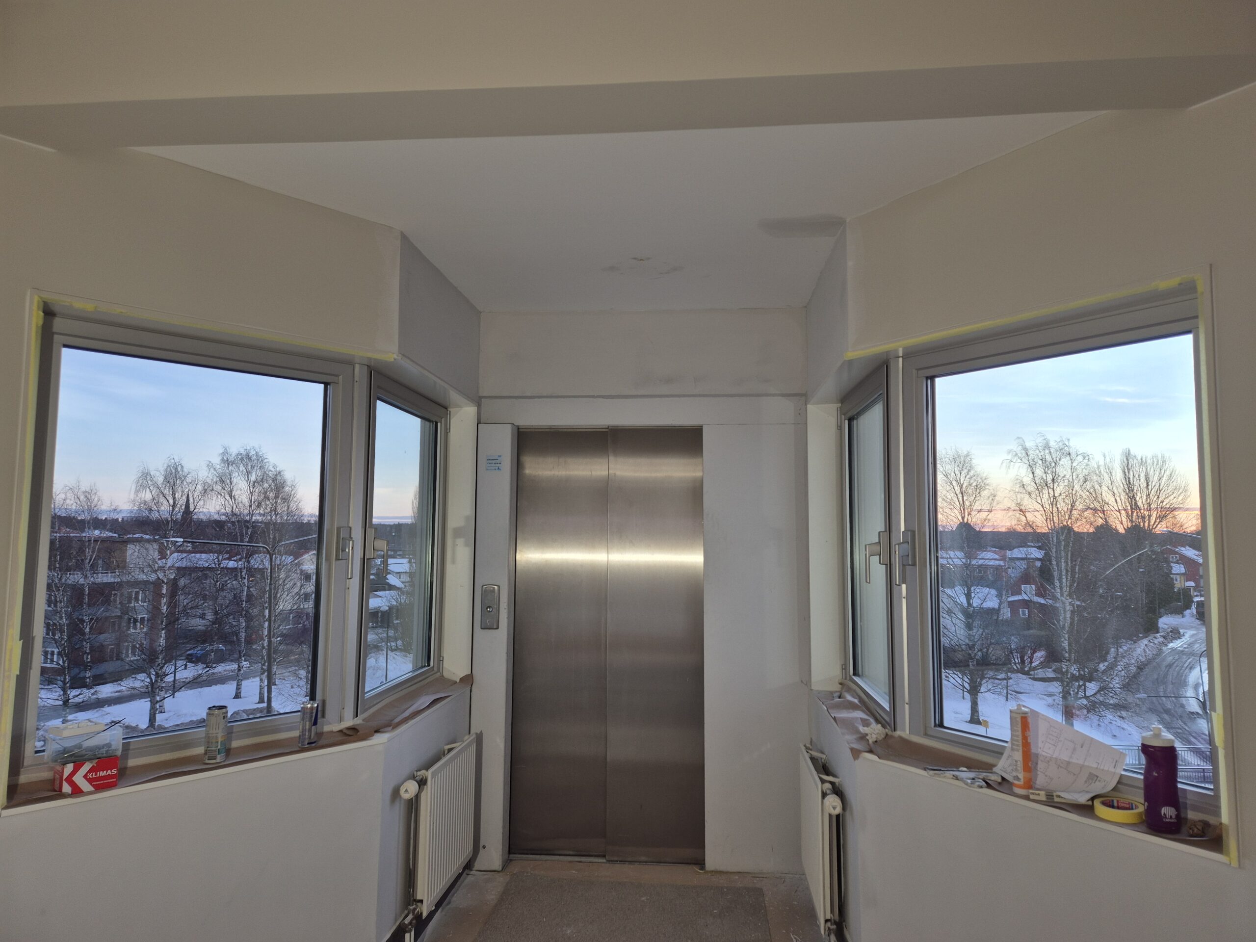 Hissdörr mellan två fönster i utrymme med pågående målningsarbete.