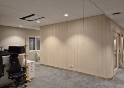 Rundad innervägg klädd i ljus träpanel i kontorsmiljö.